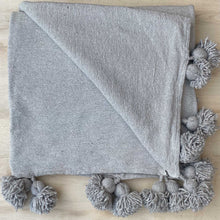 Lade das Bild in den Galerie-Viewer, Hellgraue Decke mit Bommeln liegt auf einer hellen Holz-Platte