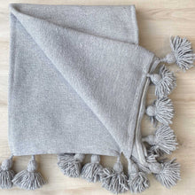 Lade das Bild in den Galerie-Viewer, Hellgraue Decke mit Bommeln liegt auf einer hellen Holz-Platte