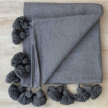 Lade das Bild in den Galerie-Viewer, Graue Decke mit Bommeln liegt auf einer hellen Holz-Platte