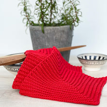 Lade das Bild in den Galerie-Viewer, Ein Paar rote gehäkelte Topflappen liegen auf einer hellen Holz-Platte mit Keramik-Schalen im Hintergrund