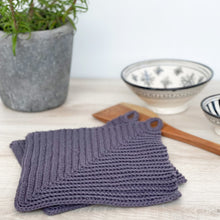 Lade das Bild in den Galerie-Viewer, Ein Paar graue gehäkelte Topflappen liegen auf einer hellen Holz-Platte mit Keramik-Schalen im Hintergrund