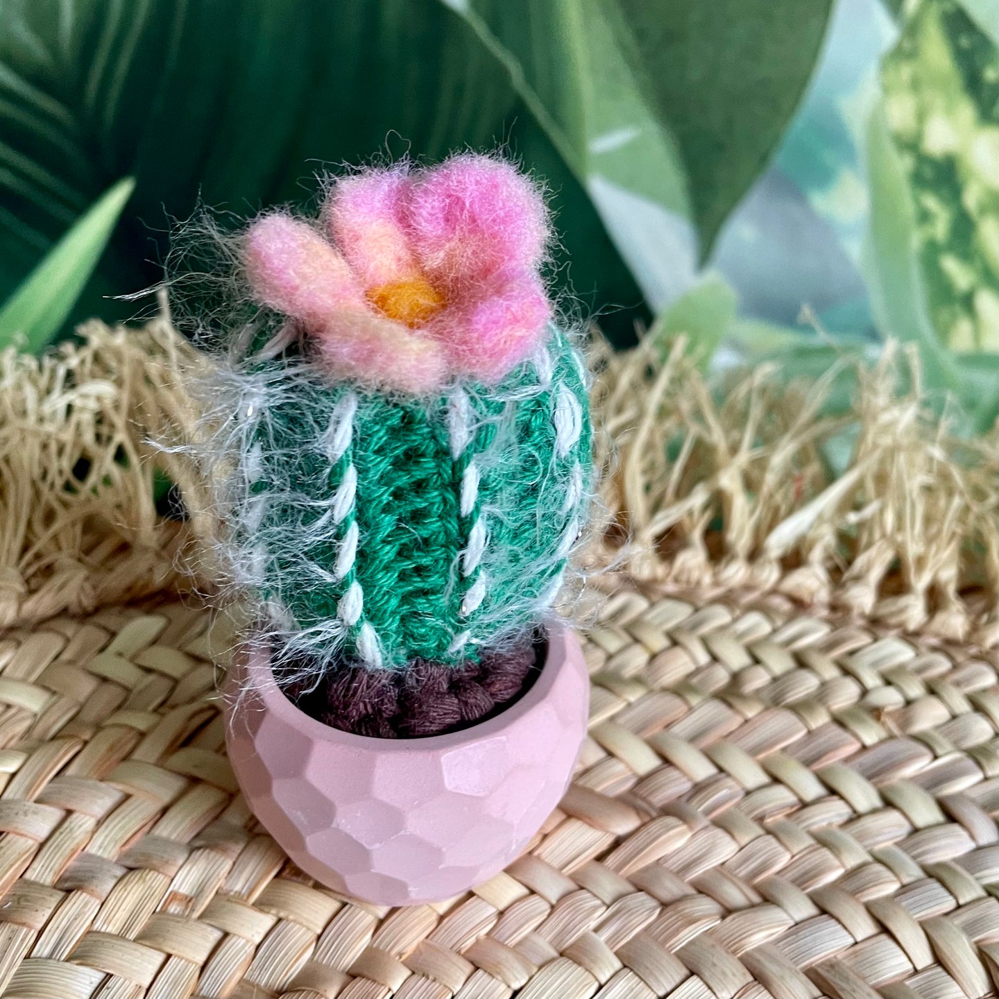Kleiner gehäkelter Kaktus im rosafarbenen Keramiktopf mit rosa-gelber Blüte. 