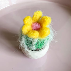 Kleiner gehäkelter Mini-Kaktus  mit gelber Blüte in einem Keramiktopf
