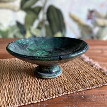 Load image into Gallery viewer, Eine marokkanische handgearbeitete grüne Keramik-Schale mit Fuß steht auf Vintage-Holztisch vor einer floralen Tapete
