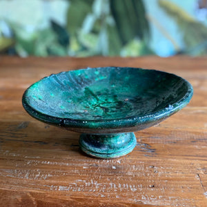 Eine marokkanische handgearbeitete grüne Keramik-Schale mit Fuß steht auf Teak-Holztisch vor einer floralen Tapete