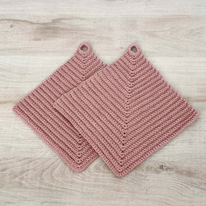 Ein Paar rosafarbene gehäkelte Topflappen liegen auf einer hellen Holz-Platte